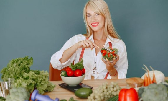 Blonde woman enjoying a fresh salad surrounded by vegetables, promoting healthy eating.